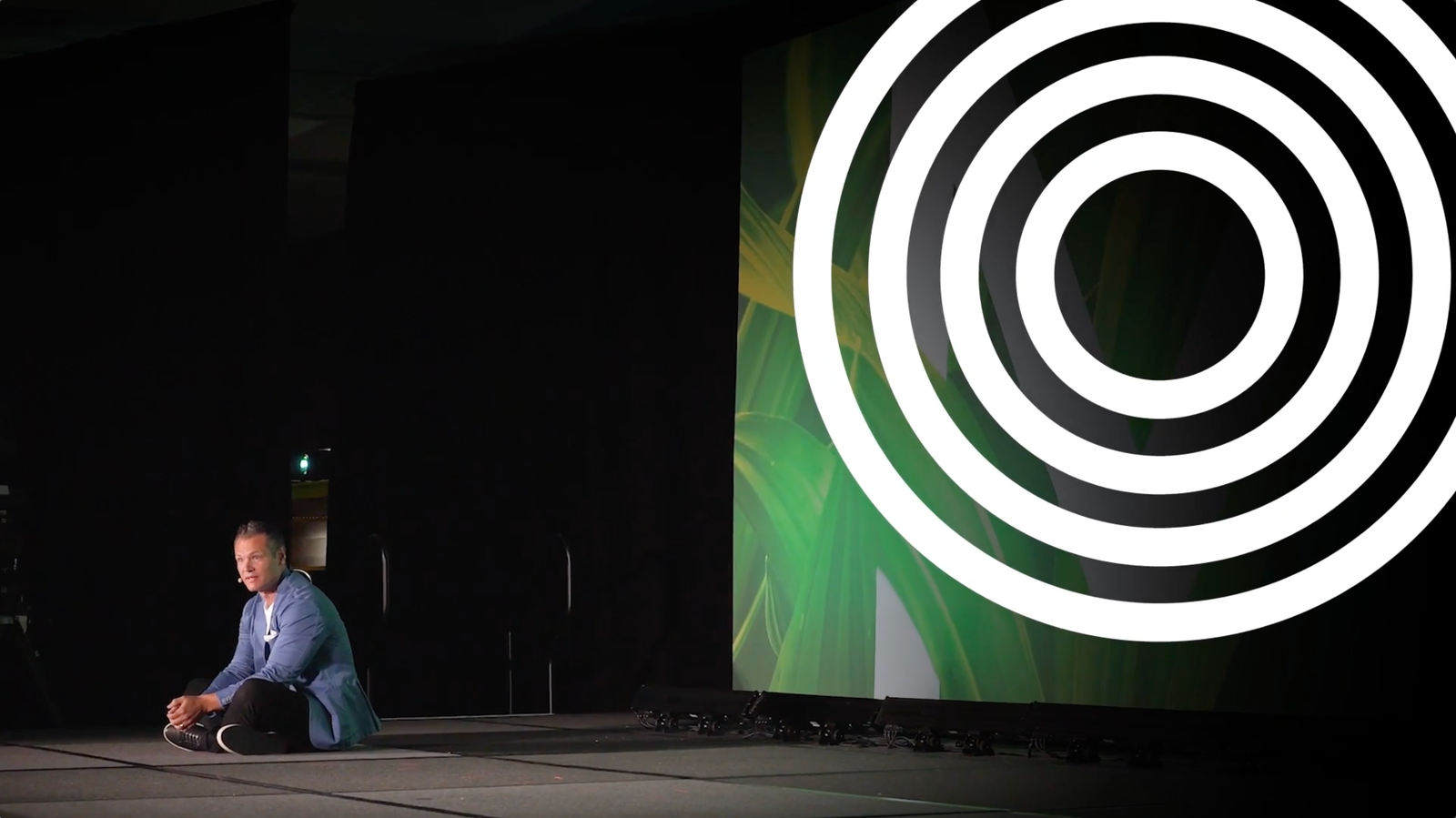 Speaker seated on the Modere conference stage in front of large animated concentric-circle graphics